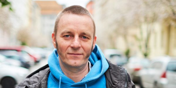 Porträtaufnahme eines Mannes mit blauem Kapuzenpullover vor verschwommenen Hintergrund