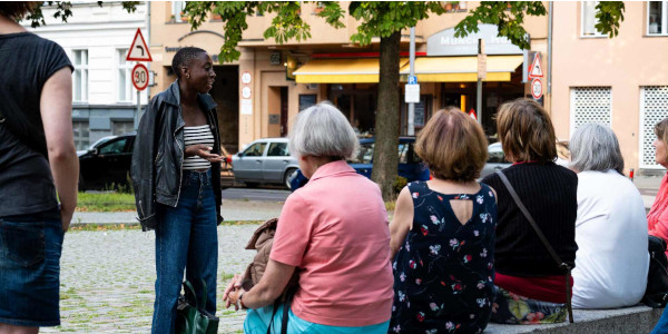 Eine Stadtführerin und Teilnehmende, die auf einer Bank sitzen