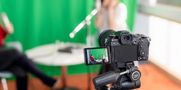 Im Vordergrund eine Videokamera und im Hintergrund verschwommen zwei Personen, die ein Interview miteinander führen