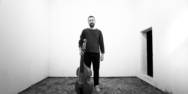 Schwarz-weiß-Foto vom Gambisten Liam Byrne mit seiner Lyra viol in einem leeren Raum