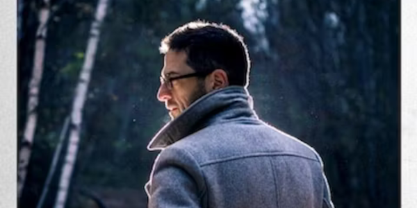 Ein Mann mit Brille und Mantel von hinten fotografiert in einem Wald