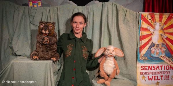 Foto einer Frau, die mit beiden Händen jeweils ein Puppen-Tier festhält. links ist ein bär. in der rechten Hand hälst sie einen Hasen