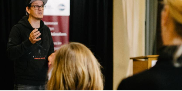 Foto eines Redners mit Cappy vor einer interessierten Zuhörerschaft