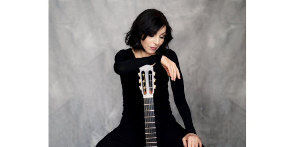 Portrait einer nachdenklich nach unten schauenden frau, die sich mit der rechten Hand auf eine Gitarre stützt