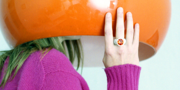 eine Frau im pinken Pullover hat einen Lampenschirm über dem Kopf.